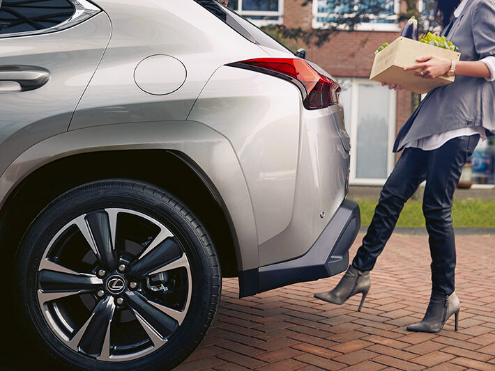 Voiture hybride Lexus UX femme qui passe son pied sous la voiture pour ouvrir le coffre