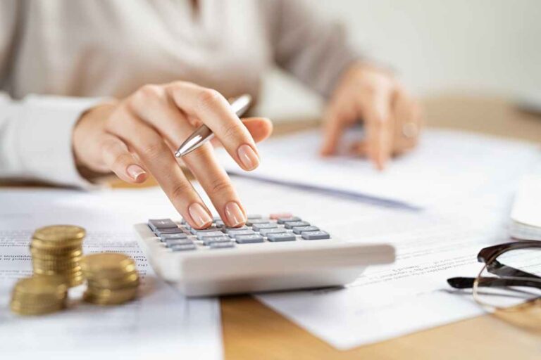 Femme assise à un bureau en bois avec des feuilles et une calculette en train de calculer la fiscalité de sa voiture de société