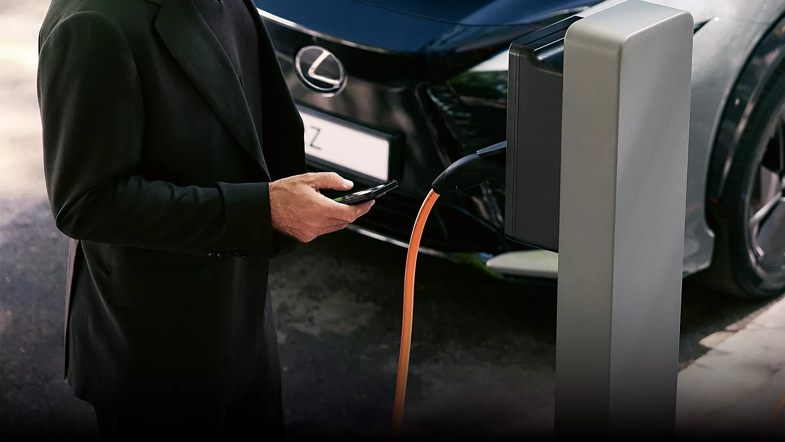 2025-lexus-rz-technology-lexus-link-keep-a-check-on-your-rz-1920×1080-250728 Homme devant une borne de recharge pour Lexus électrique